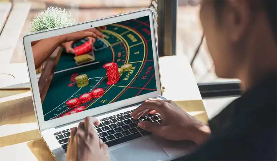 Player playing baccarat online on a laptop with chips and cards on the desk